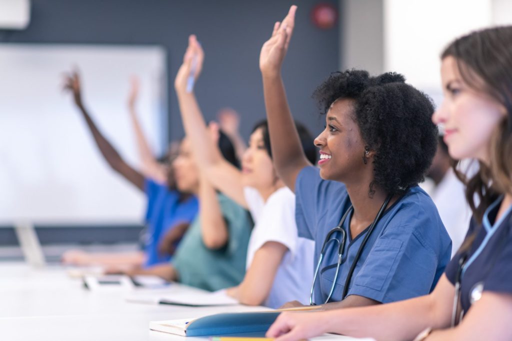 Healthcare staff in scrubs raising their hands during a training session
