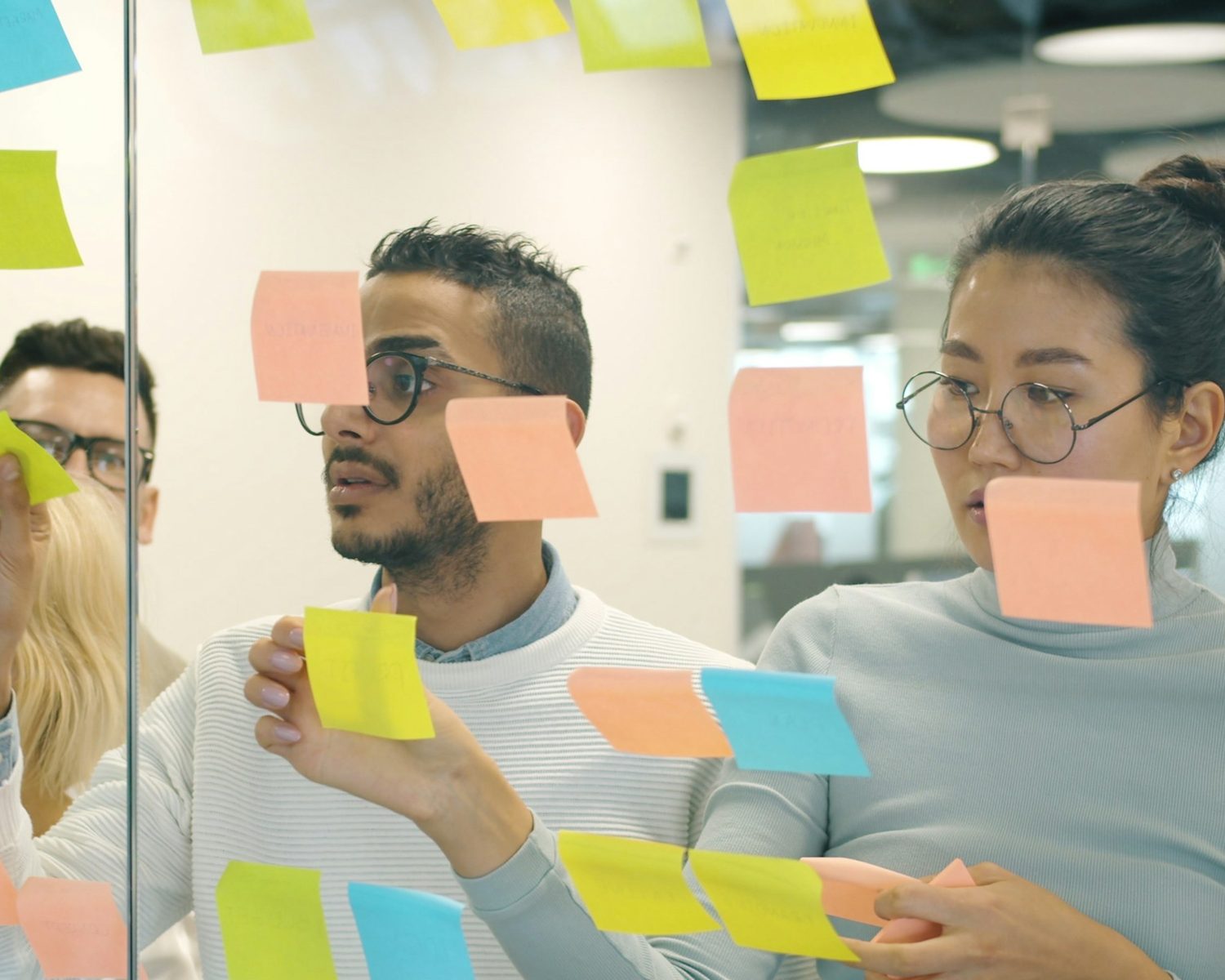 The innovation process at work: a team at a glass wall of ideas, one colleague placing a note